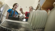 Young girls fill the dishwasher with dirty dishes