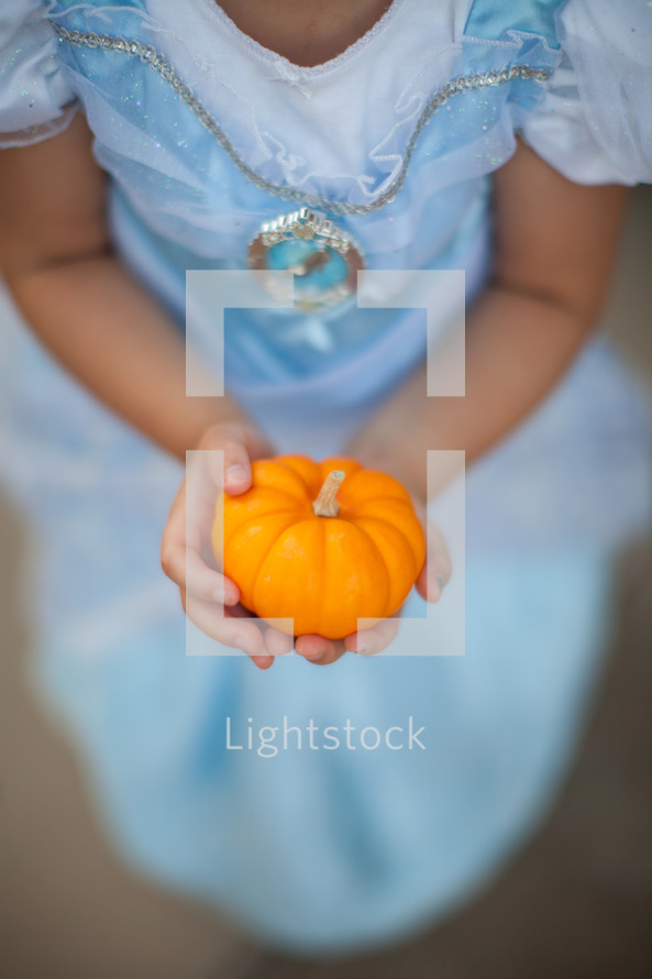 a girl in a princess costume holding a pumpkin 
