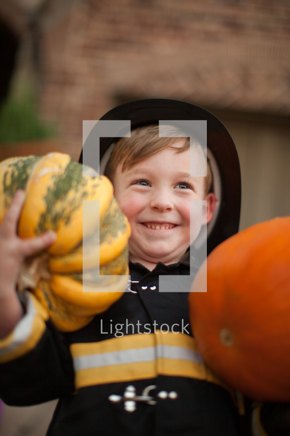 a boy child in a costume holding a pumpkin