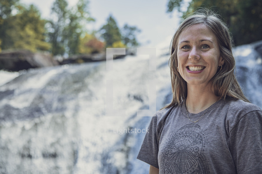 smiling woman standing in front of a waterfall 