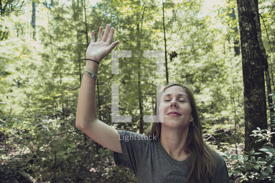 woman alone in a forest with hand raised 