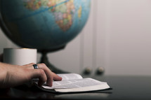 a man reading a Bible and globe on a desk 