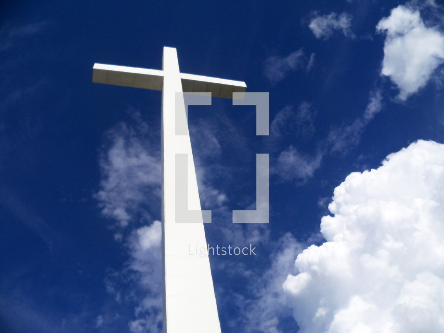 A large white cross stretches out against a blue sky surrounded by clouds and the earth's atmosphere as it stretches out between Heaven and Earth to show the power and reach of the gospel message to all the earth that Jesus was crucified, died then resurrected from the dead three days later overcoming the grave, death and sin for all of mankind for all ages. 