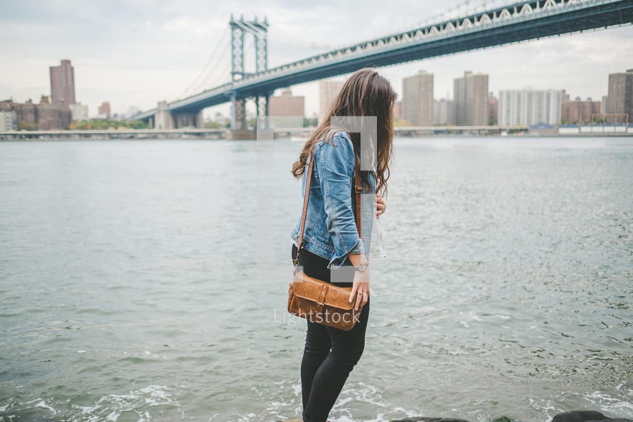 a woman with a purse walking along the shore in NYC 