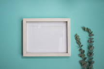 Blank white frame on turquoise background with eucalyptus