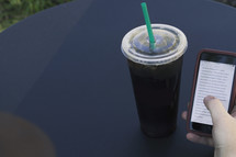 a man looking at a cellphone screen and iced soda
