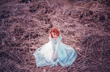 a woman sitting in a field in a long dress