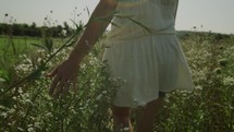 a woman touching talk grasses as she walks though a field 