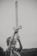a boy in a crown holding up a wooden sword 