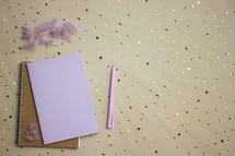 Notebooks with pen and flowers over the brown background. 