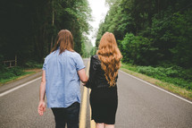 A man and woman walk down a highway lined with trees.