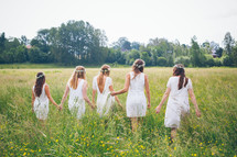 bridesmaids walking hand in hands through a field 