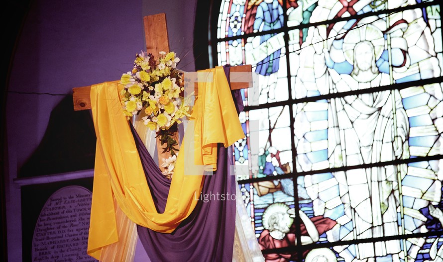 Veiled cross with a floral wreath in front of a stained glass window.