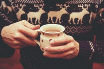a man in a winter sweater holding hot chocolate 