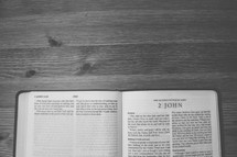 Bible on a wooden table open to the book of 2 John.