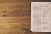 Bible on a wooden table open to the book of 2 Samuel.