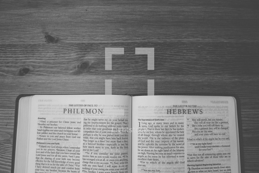 Bible on a wooden table open to the Letter of Paul to Philemon and the Letter to the Hebrews.