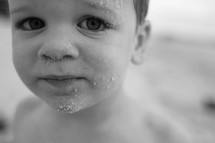 A little boy with sand on his face.