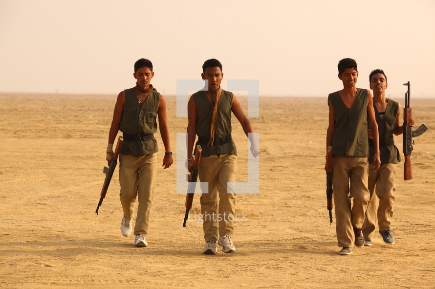 young men walking with rifles through the desert 