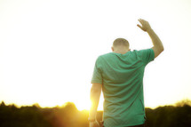 A man, with hand raised, worshipping at sunrise