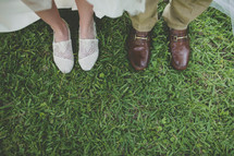 two pairs of feet in shoes standing in the grass after their wedding