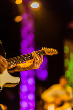 Hands playing electric guitar on lighted stage durning worship