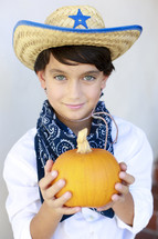boy in a cowboy costume holding a pumpkin