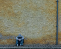 man in a hoodie sitting on a brick sidewalk with his head down