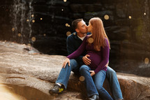 man kissing a pregnant woman sitting on rocks