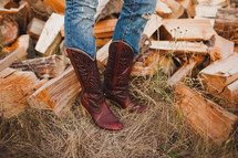 Woman in cowboy boots by chopped wood