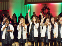 A group of female and male singers sing a chorus of praise during a Christmas praise and worship concert wearing white blazers and sparkling dresses while singing during a church Christmas concert. These are the voices of Mobile - a praise and worship group from Mobile Alabama singing at a Christmas concert along with the church choir at a recent praise and worship event. 