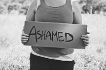 woman holding a sign that reads ASHAMED