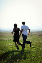 Man and woman in boots running across grassy field.