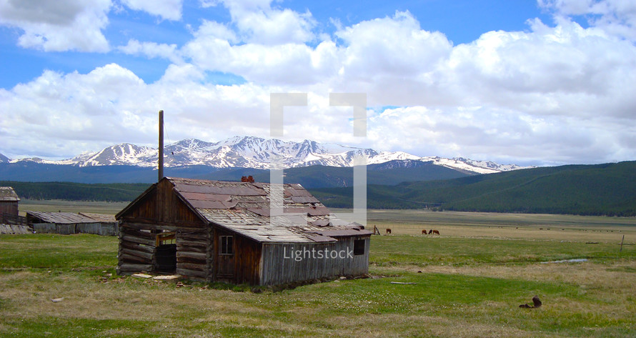 Log cabin in a field surrounded by mountains