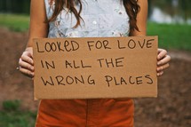 woman holding a sign with the words LOOKED FOR LOVE IN ALL THE WRONG PLACES