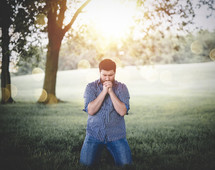 man kneeling in a park praying 
