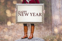 a woman holding a sign the reads Happy New Year 