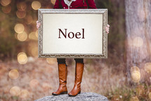 a woman holding a sign the reads Noel 