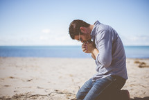 man kneeling on a beach praying 
