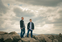 two men standing on rocks on a mountaintop 