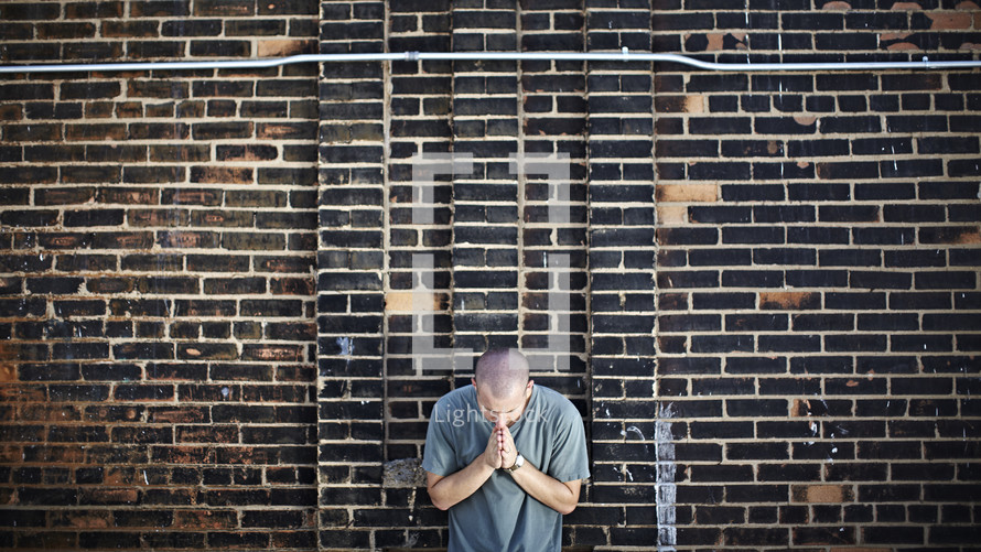 Man praying in front of brick wall