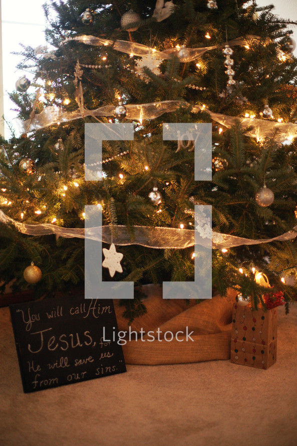 A Christmas tree with a chalk board that reads, 'You will call his name Jesus'