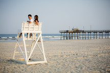 couple sitting together on a lifeguard stand on a beach