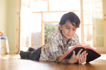 A child lying on the floor and reading the Bible.
