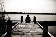 A man sitting on a dock looking out at the water