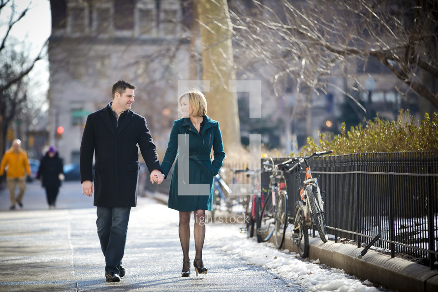 couple walking holding hands on a sidewalk 