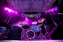 A backstage view of drums on a stage lit by purple lights