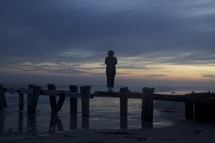woman standing on the pillars of a broken pier