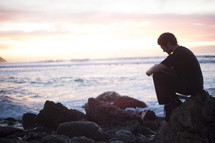 Man sitting on rock by beach in prayer