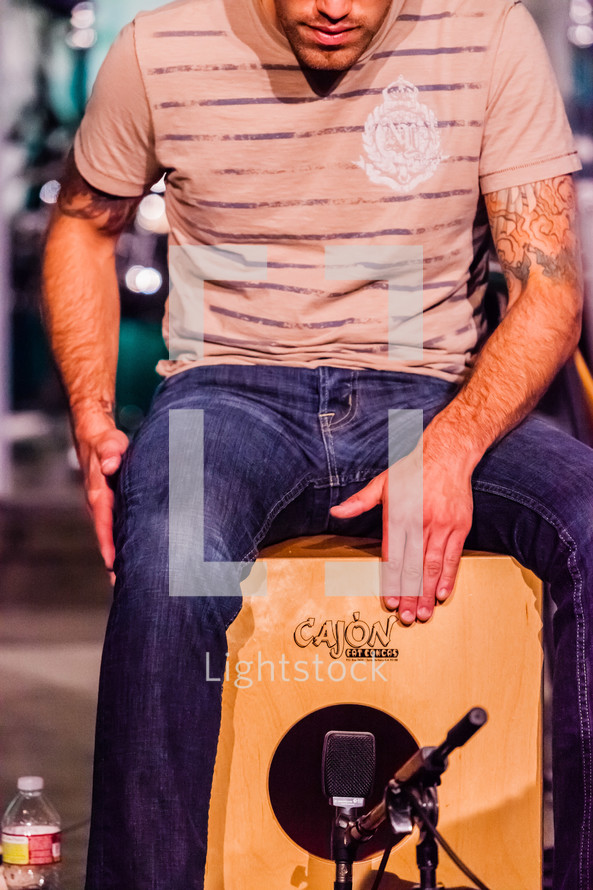 Man sitting on a wooden box playing cajon hands hitting drum percussion